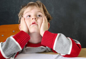 Child sitting in a desk, hands on face. Looks overwhelmed